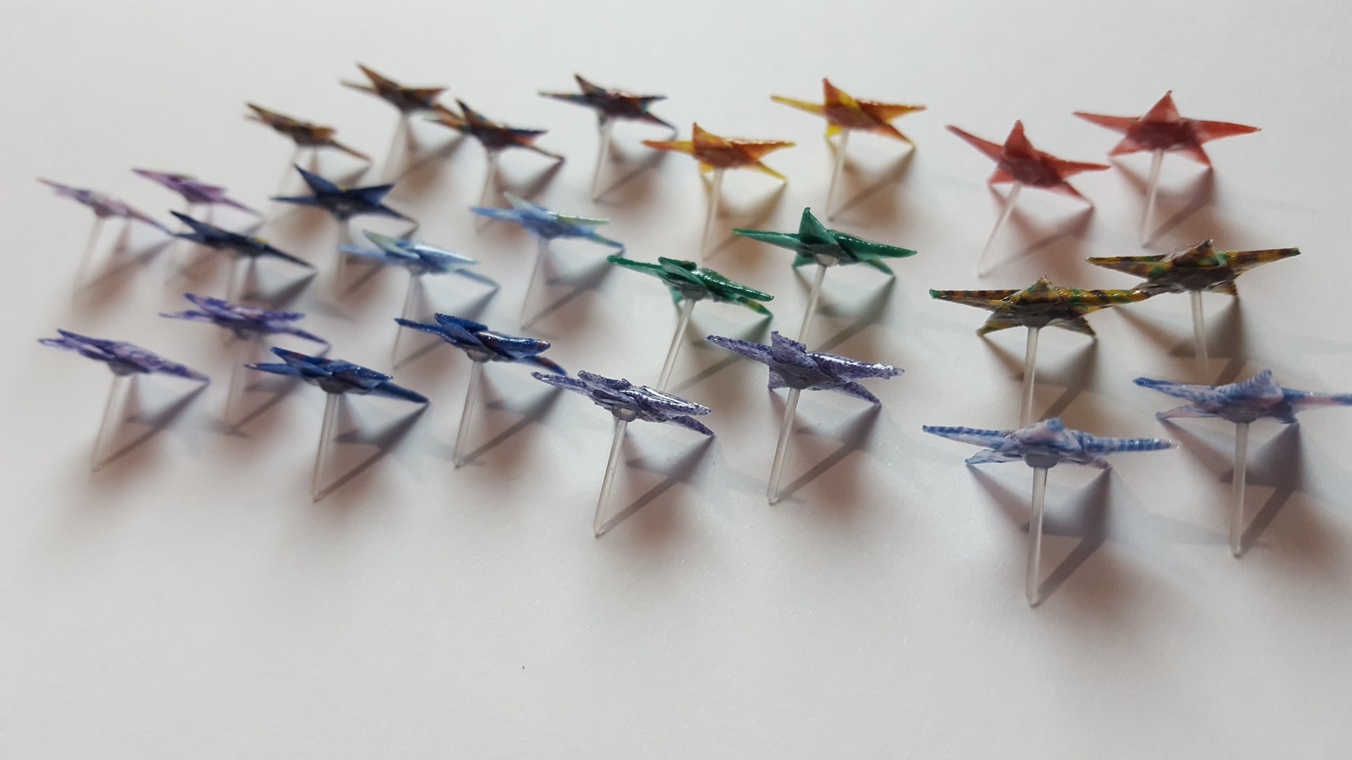 Colorful paper star-shaped stud earrings arranged in rows on a white background. 