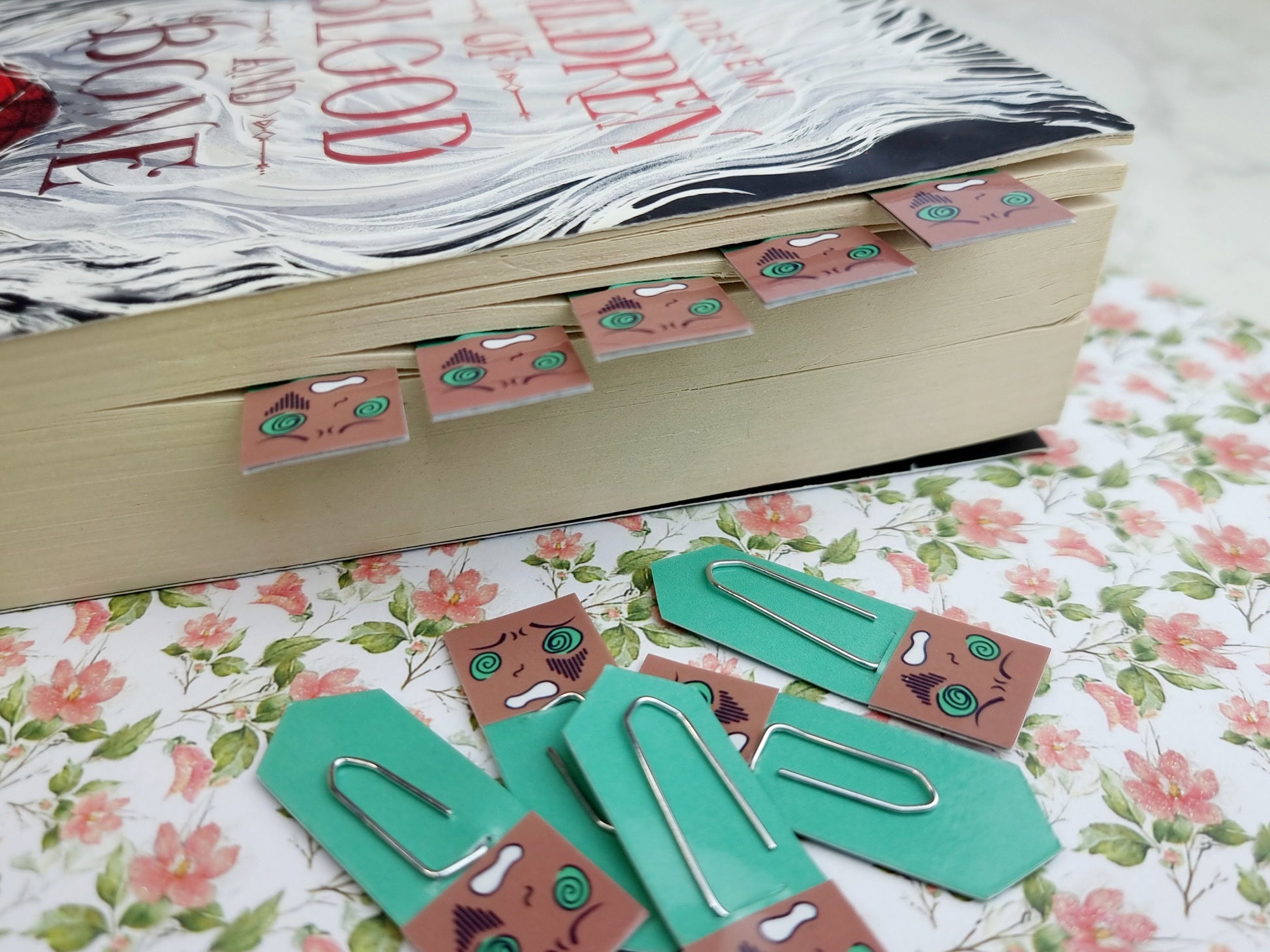 Book with decorative paper clips on a floral surface.